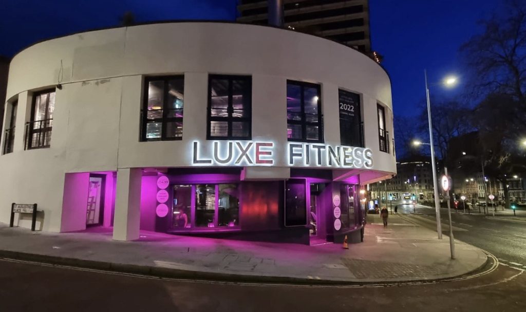 a picture of luxe gym lit up in white lights with pink lighting over the entrance